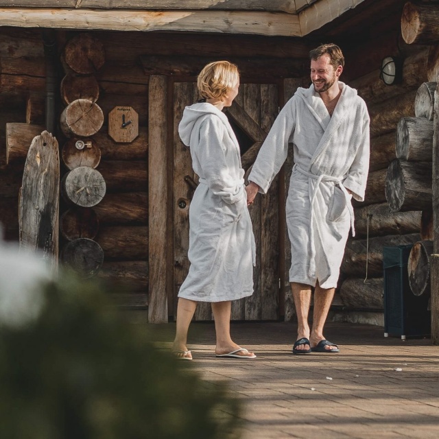 Pärchen in Bademänteln vor einer Blockhaus-Sauna